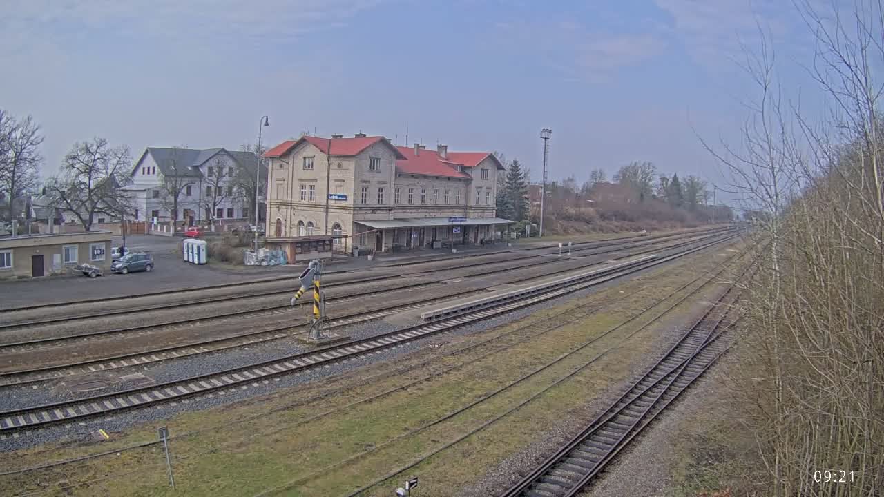 A train station with a long platform and multiple train tracks, situated in a town under a mostly cloudy sky.
