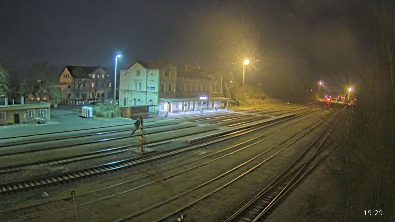 A nighttime view of a train station with multiple train tracks extending into the distance under hazy, dimly lit conditions.