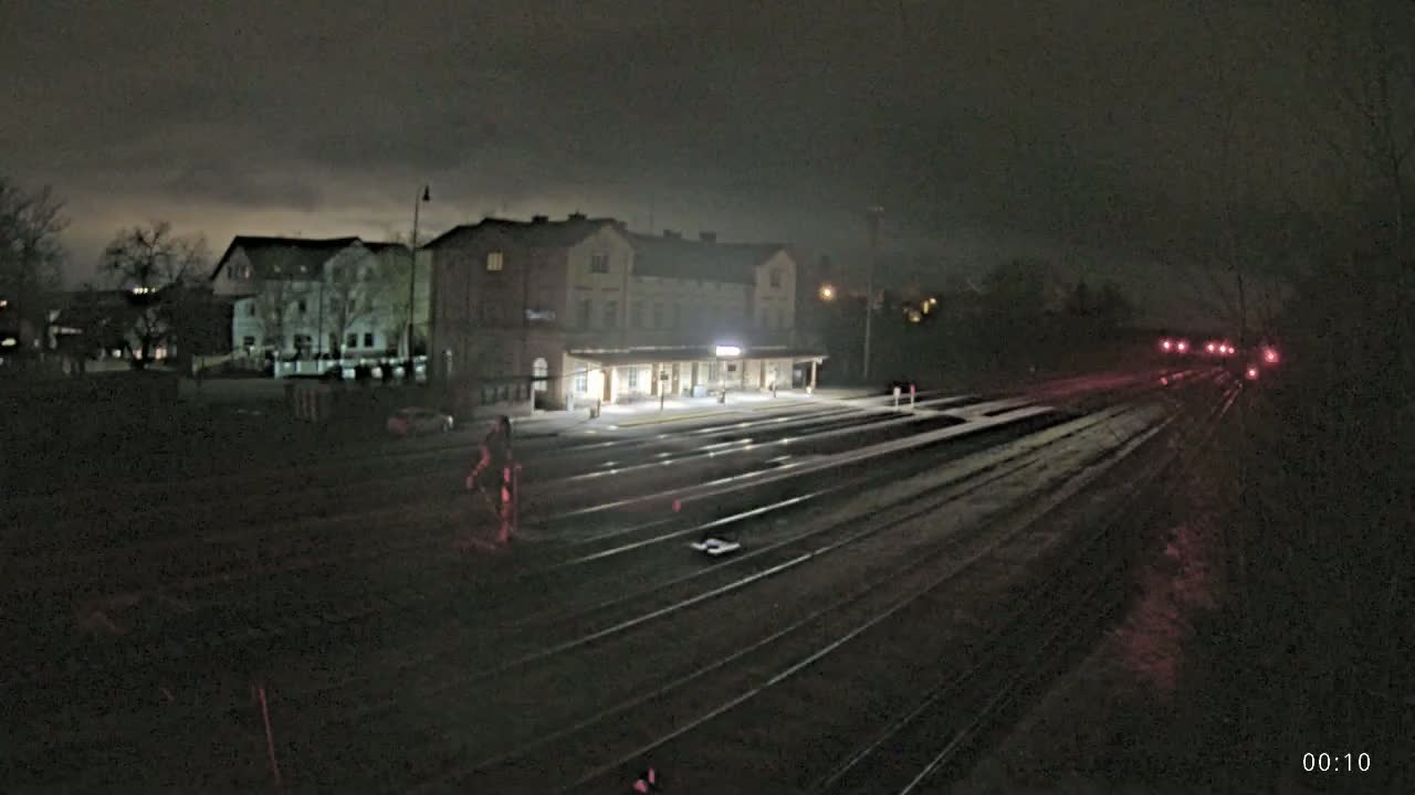 A train station at night under a dark, cloudy sky, with several tracks extending into the darkness.