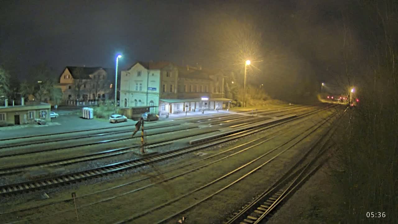 A nighttime view of a train station with several tracks extending into the distance under hazy, dimly lit conditions.