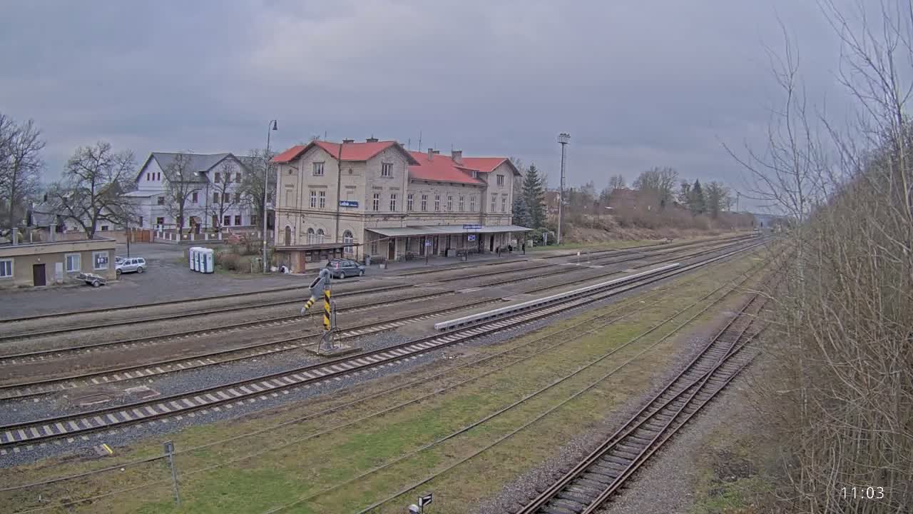 A train station with a long platform and several train tracks stretches into the distance under an overcast sky.