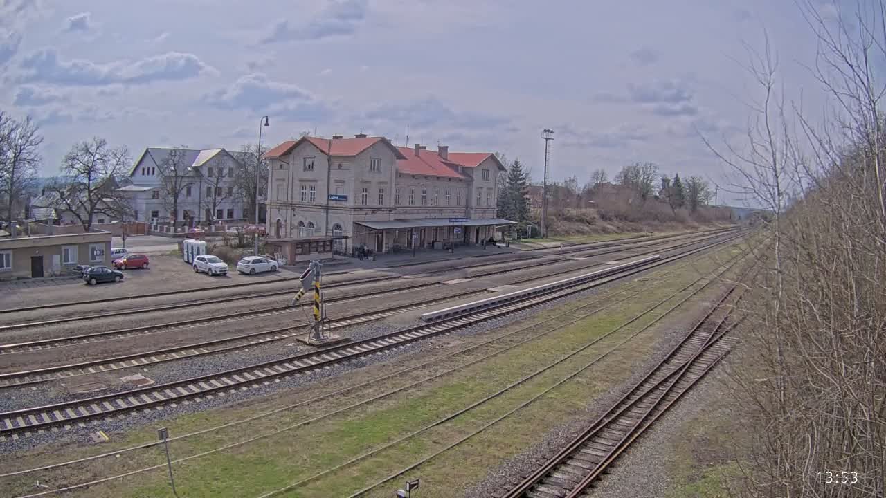 A long view of a train station with a large building and several tracks under a partly cloudy sky.