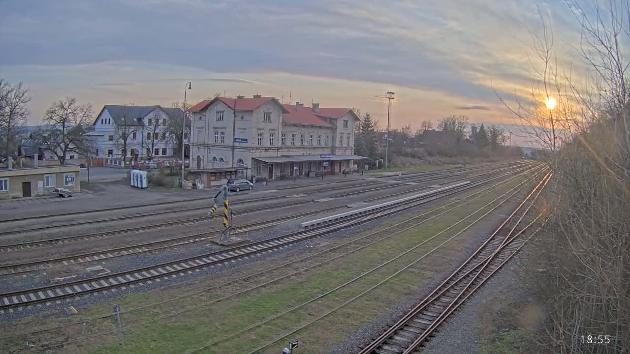 A long view of a train station with multiple train tracks extending into the distance under a partly cloudy sunset.