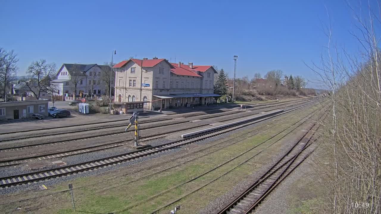 A train station with a long platform and multiple train tracks stretches into the distance under a clear blue sky.