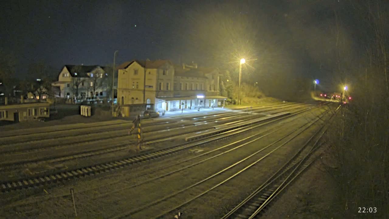 A nighttime view of a train station with multiple tracks extending into the distance, illuminated by artificial lights under a clear, dark sky.