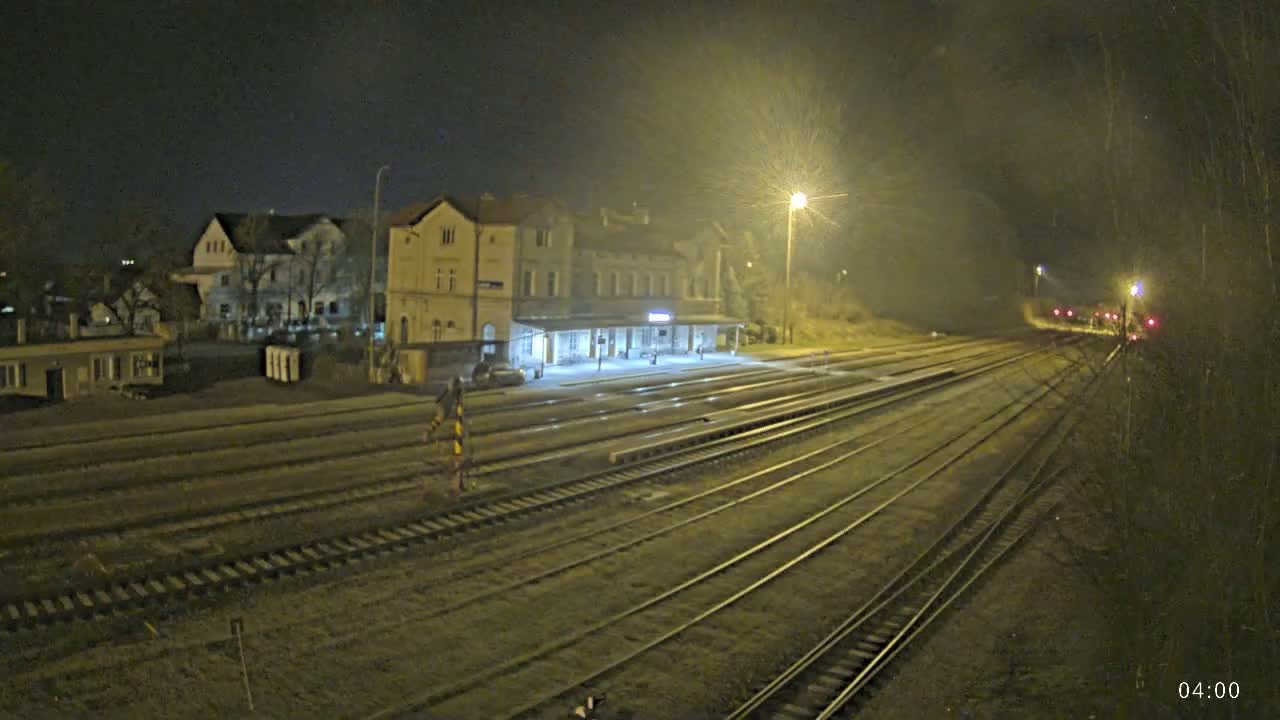 A nighttime view of a train station with multiple train tracks extending into the distance under hazy, poorly lit conditions.