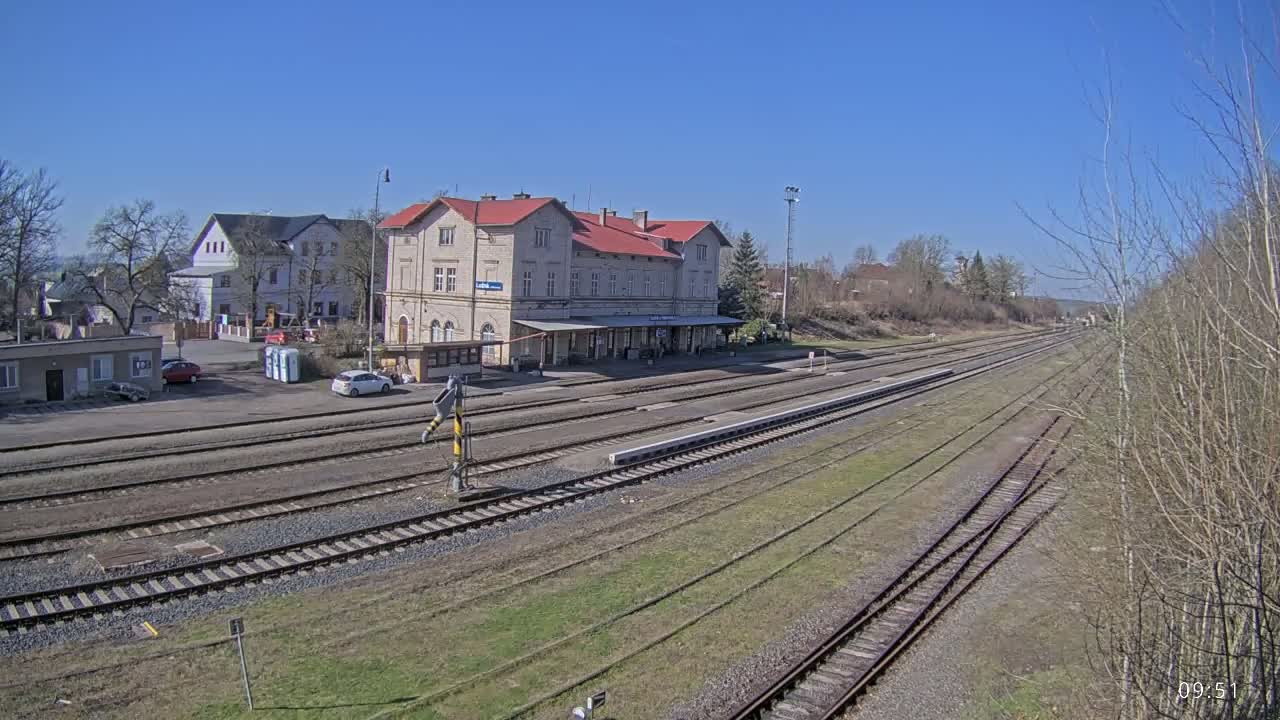 A long view of a train station with a large building and multiple train tracks under a clear blue sky.