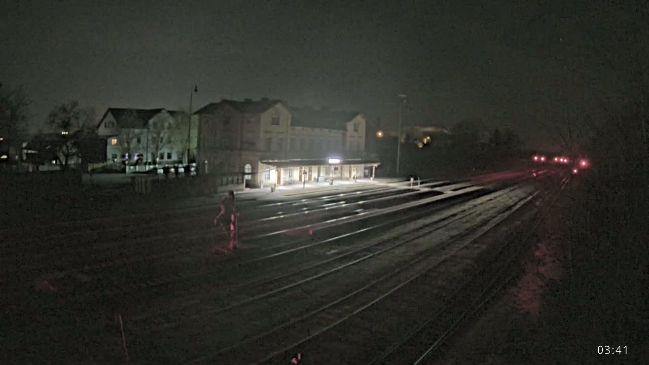 A nighttime view of a train station with several tracks and a few lights visible in the distance, under a dark sky.