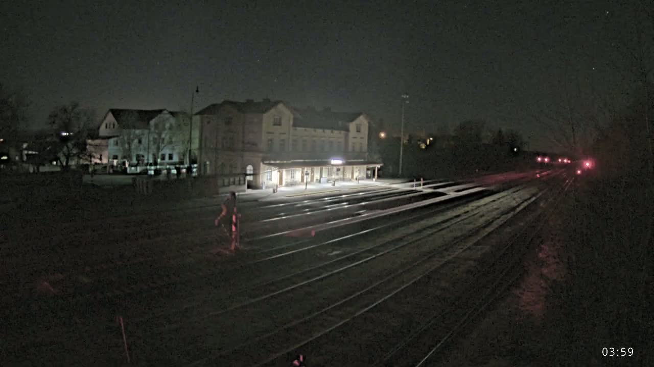 A nighttime view of a train station with a long set of tracks extending into the darkness, and a train visible in the distance.