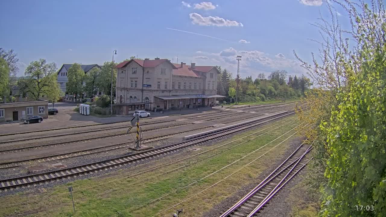 A train station with a long building and several train tracks, under a mostly sunny sky.