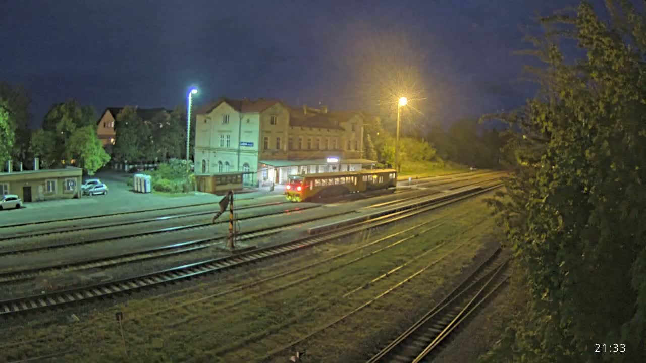 A train is stopped at a station at night, under partly cloudy skies, next to a large building.