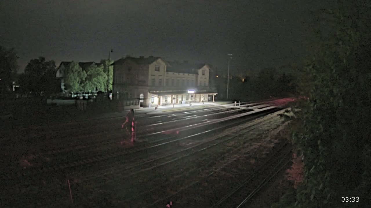 A brightly lit train station stands under a dark night sky, with train tracks extending into the darkness.
