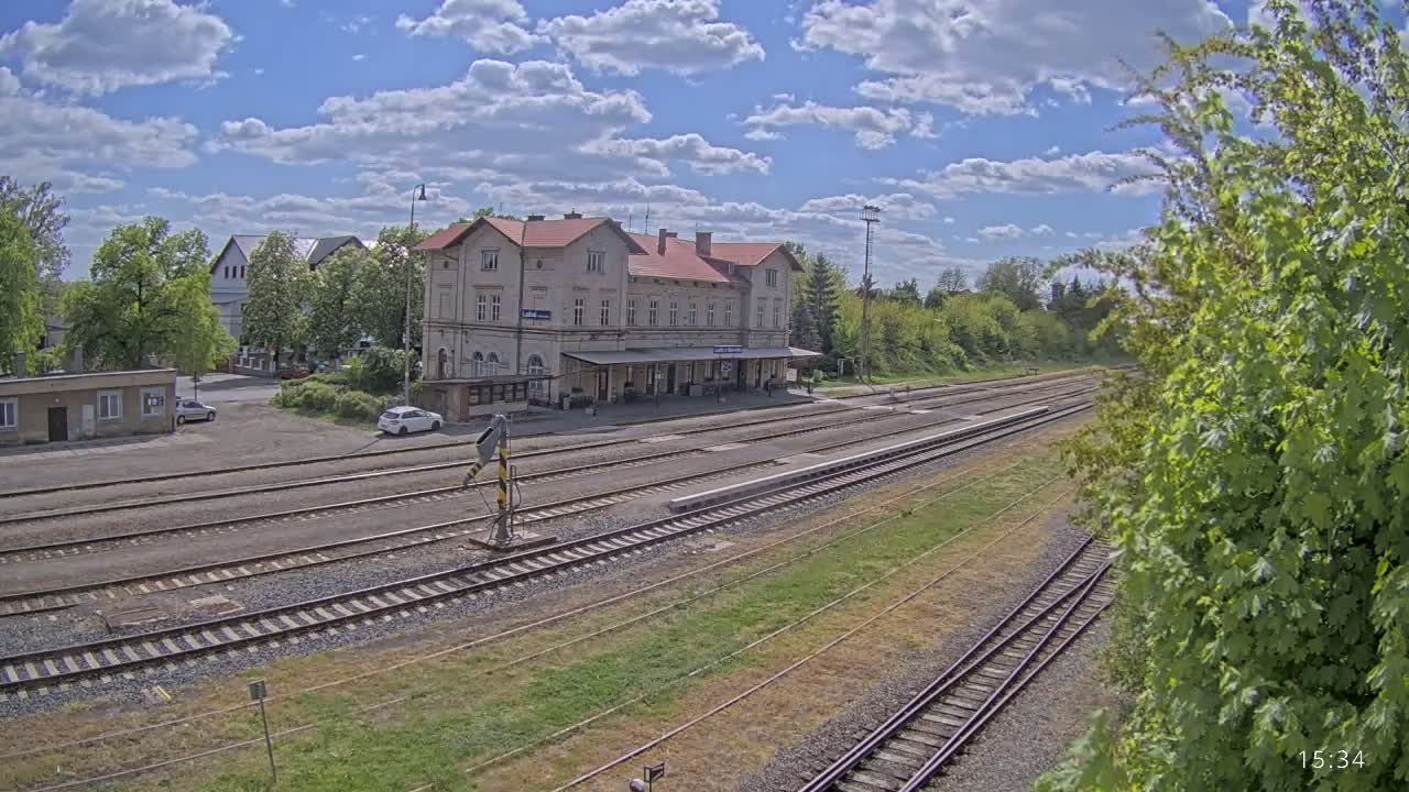 A train station with a long platform and multiple train tracks sits under a partly cloudy sky.
