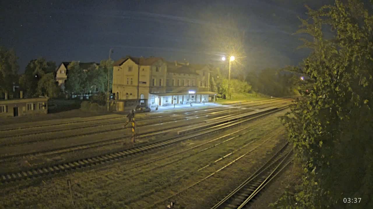 A train station at night, illuminated by artificial lights, with multiple train tracks extending into the distance under a clear, dark sky.