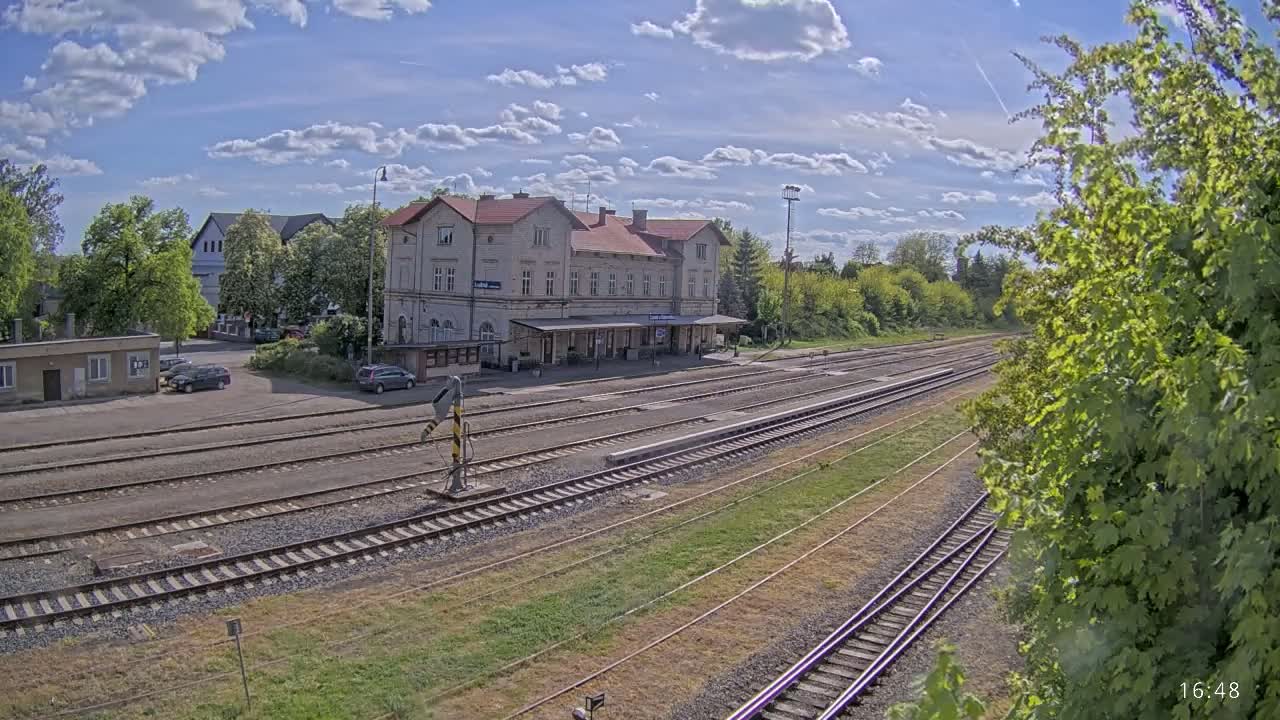 A train station with a long platform and multiple train tracks sits under a partly cloudy sky.