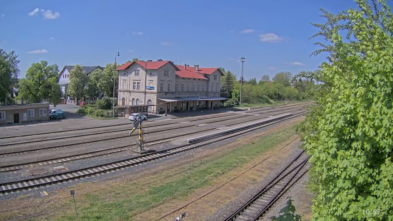 A train station with a long platform and several train tracks sits under a mostly sunny sky.