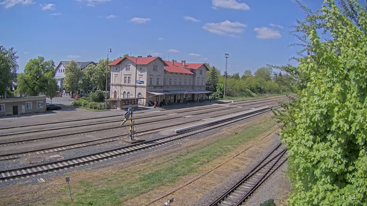 A train station with a long platform and several train tracks sits under a mostly sunny sky.