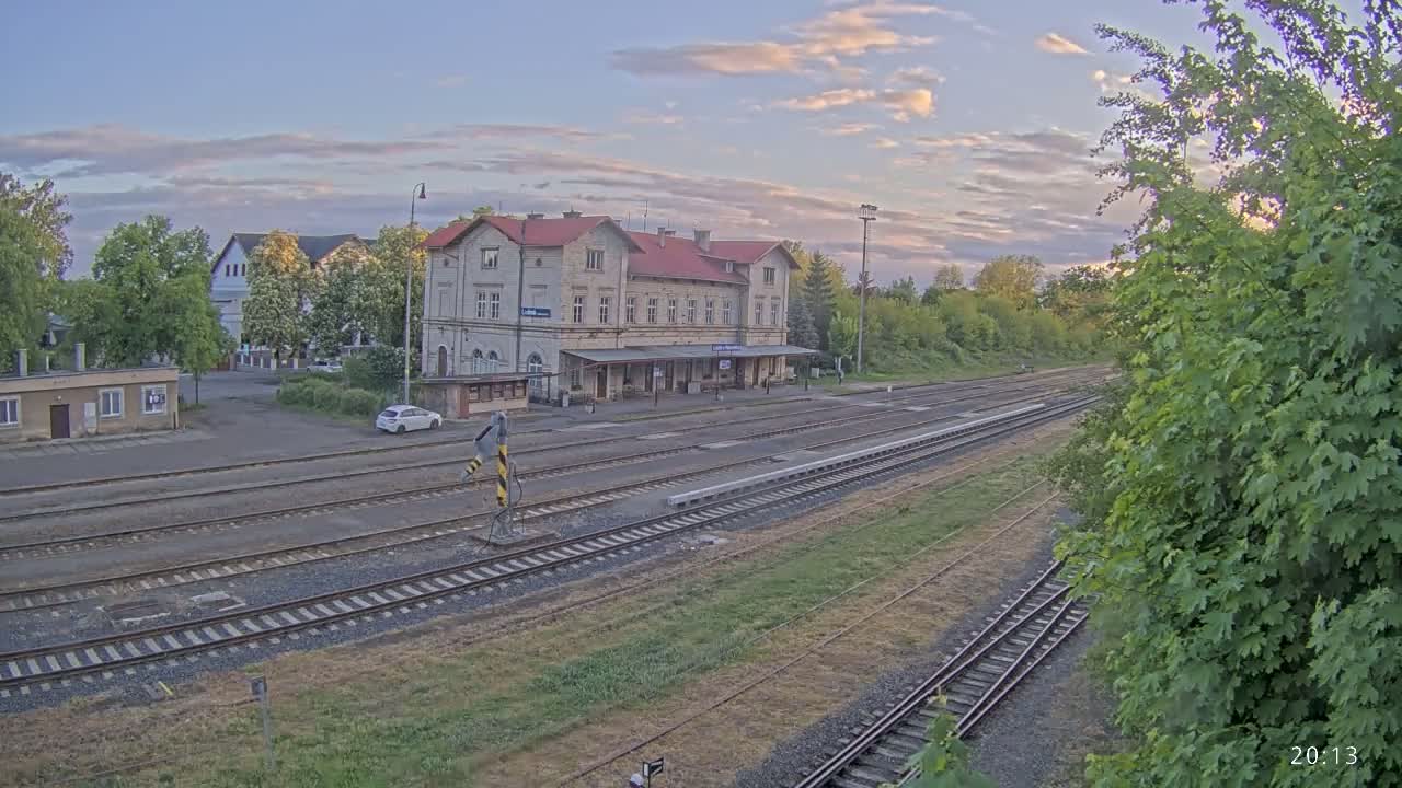 A long, low train station building sits beside several train tracks under a partly cloudy, twilight sky.