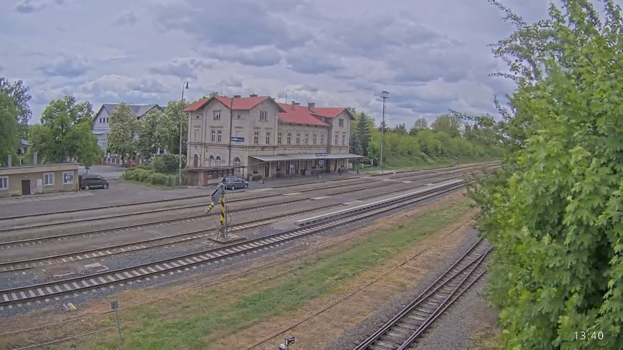 A train station with a long, low building and several tracks sits under a cloudy sky.
