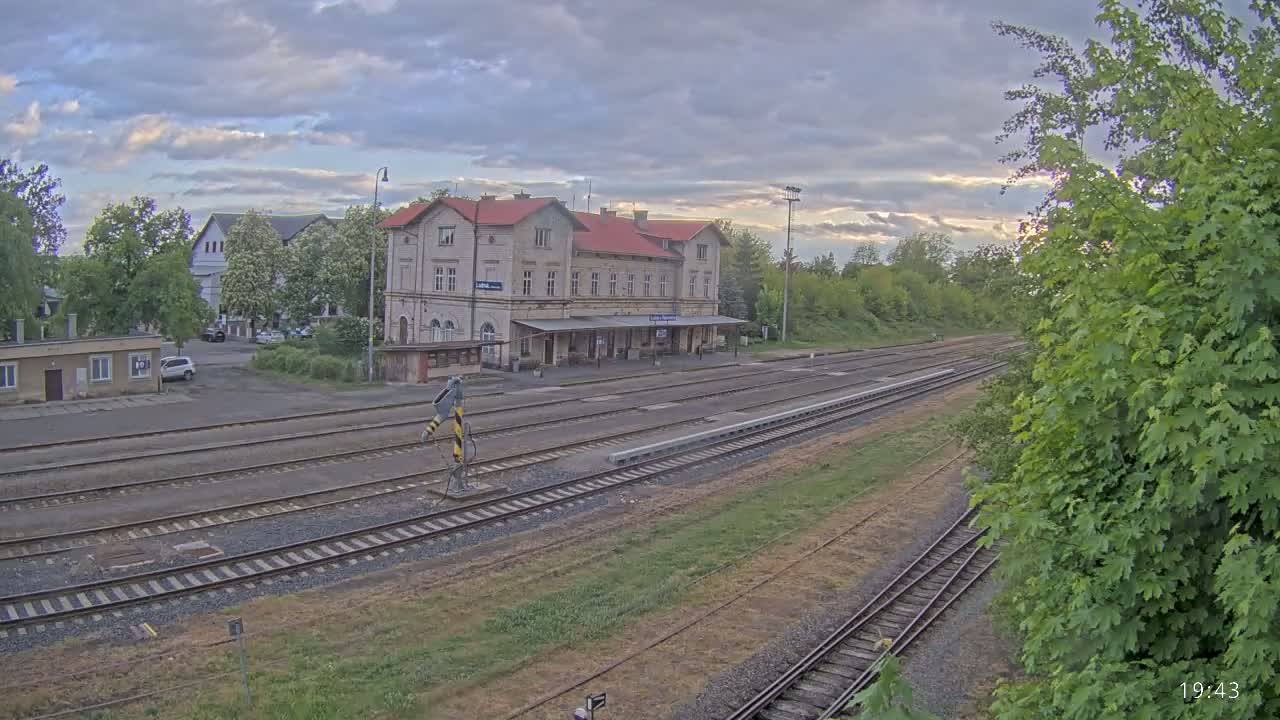 A train station with a long platform and multiple train tracks under a partly cloudy sky.