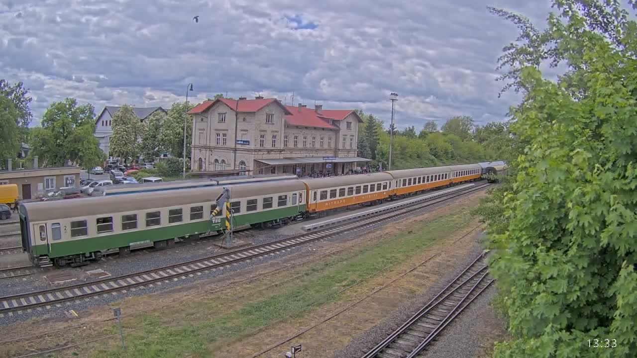 A long passenger train is at a station under a partly cloudy sky.
