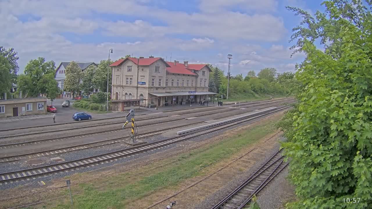 A long view of a train station with a red-roofed building, several train tracks, and a partly cloudy sky.