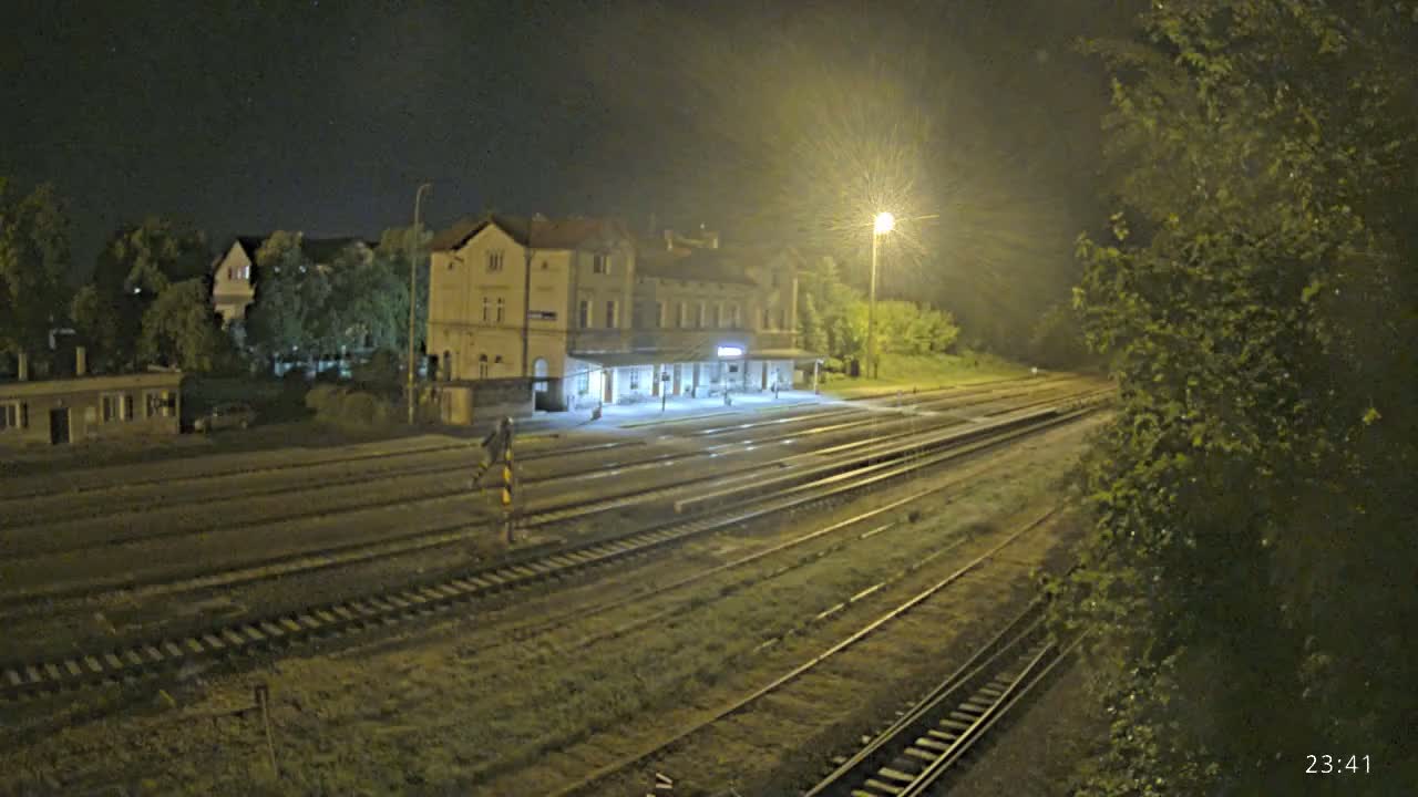 A train station at night, illuminated by a single lamp, with multiple train tracks extending into the darkness.