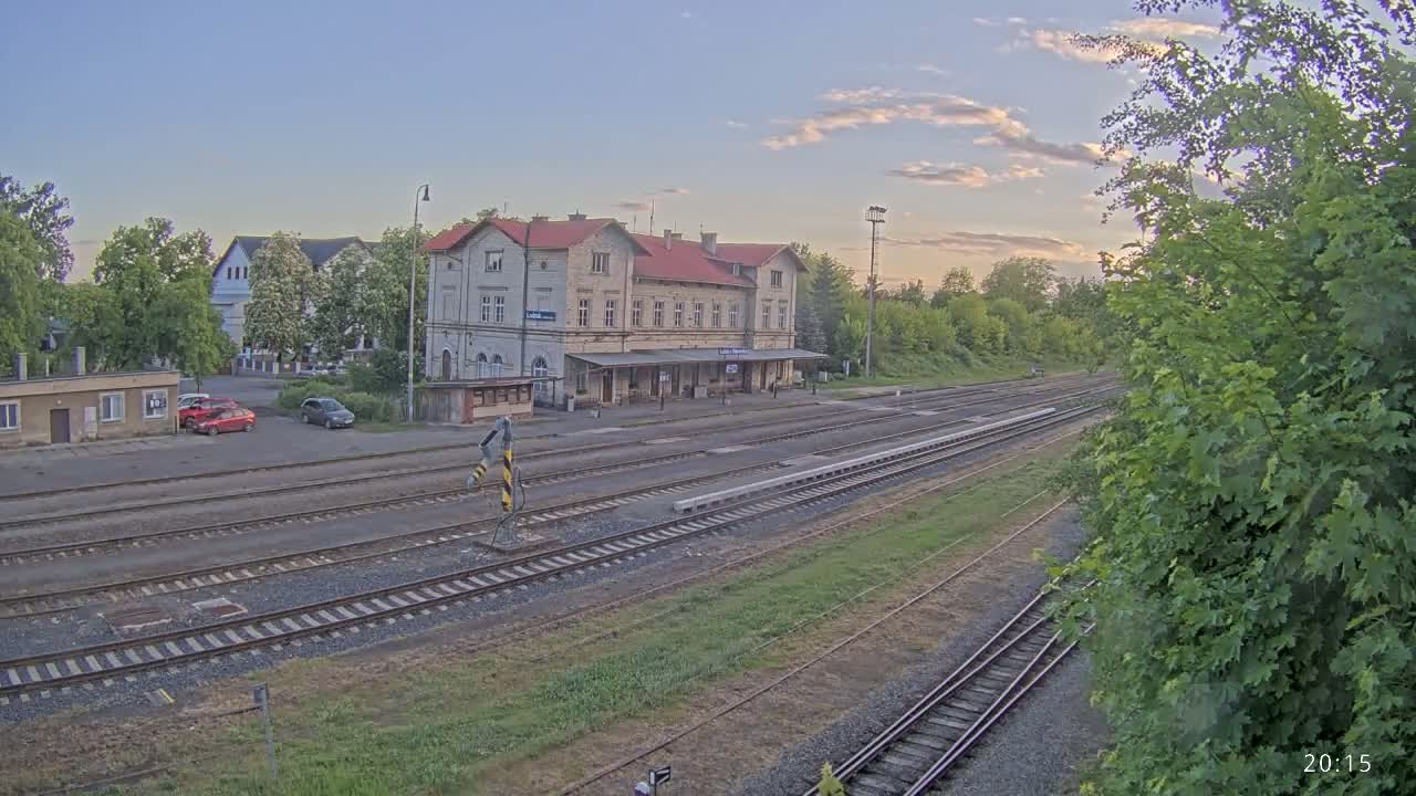 A train station with a long platform and several train tracks sits under a partly cloudy evening sky.