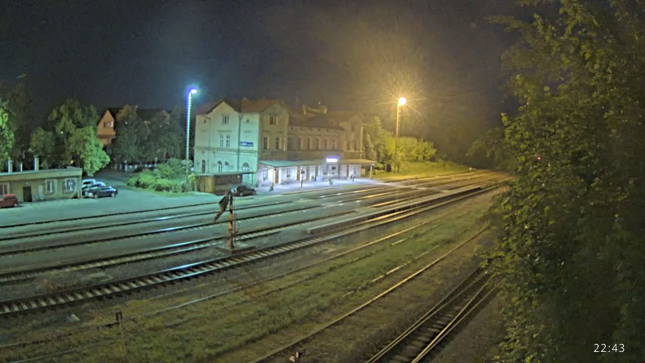 A nighttime view of a train station with multiple train tracks extending into the distance, illuminated by artificial lights under a dark sky.