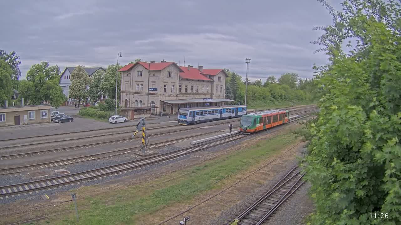 A train station with two trains, one blue and one green, sits under an overcast sky.