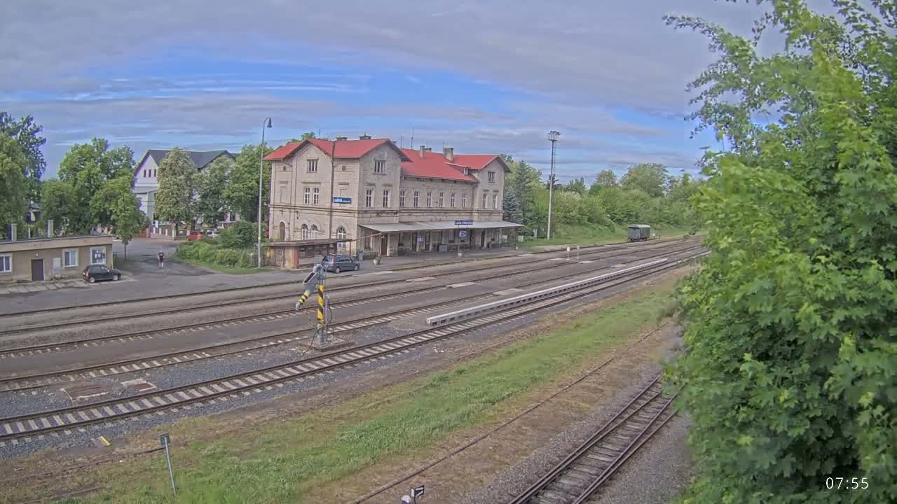 A train station with a long building and multiple train tracks, under a partly cloudy sky.