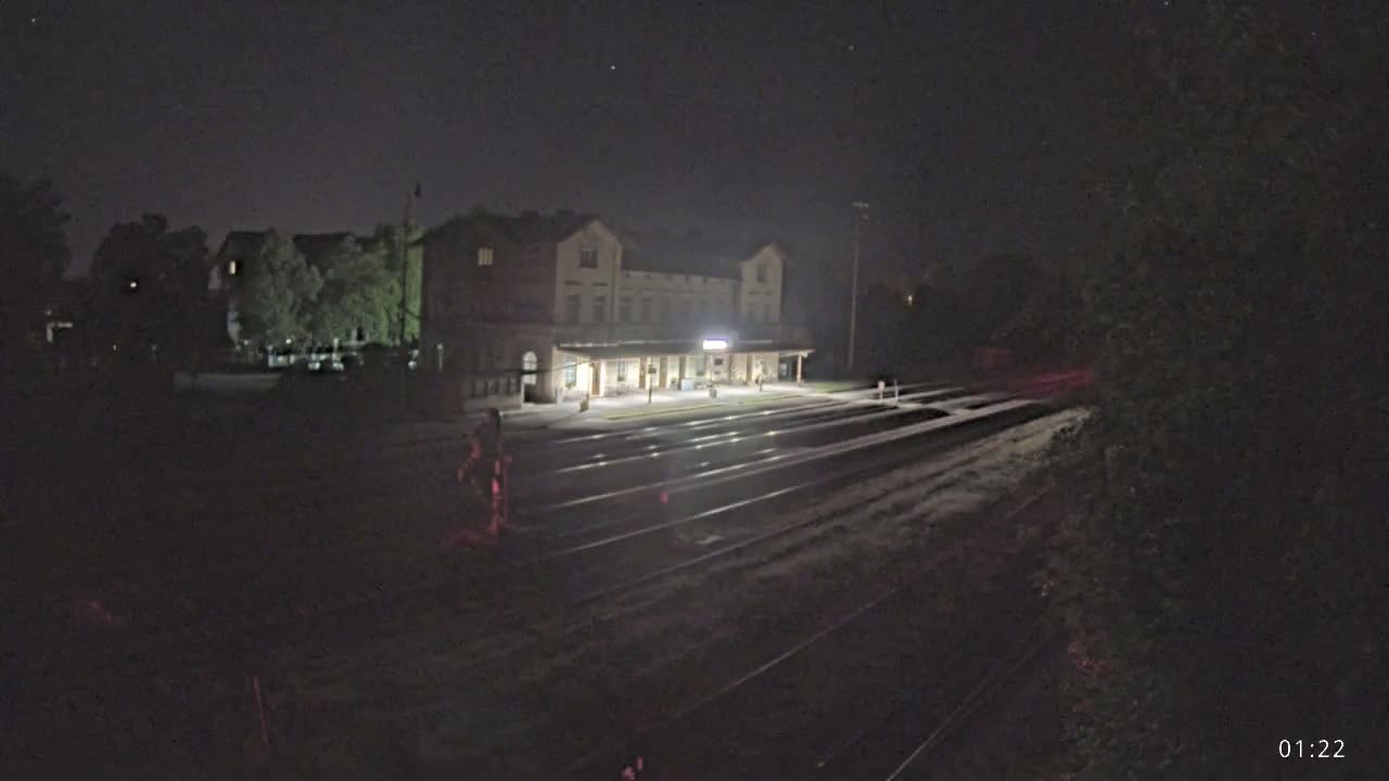 A long, low building, possibly a train station, is illuminated at night next to train tracks.