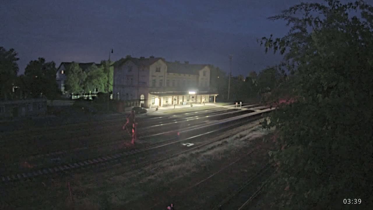A brightly lit train station at night is situated beside a rail yard under a dark sky.