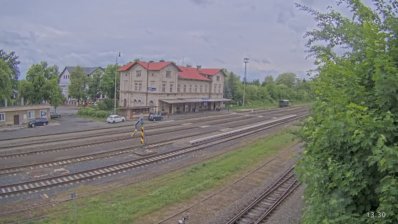 A train station with a long, red-roofed building sits beside multiple train tracks under an overcast sky.