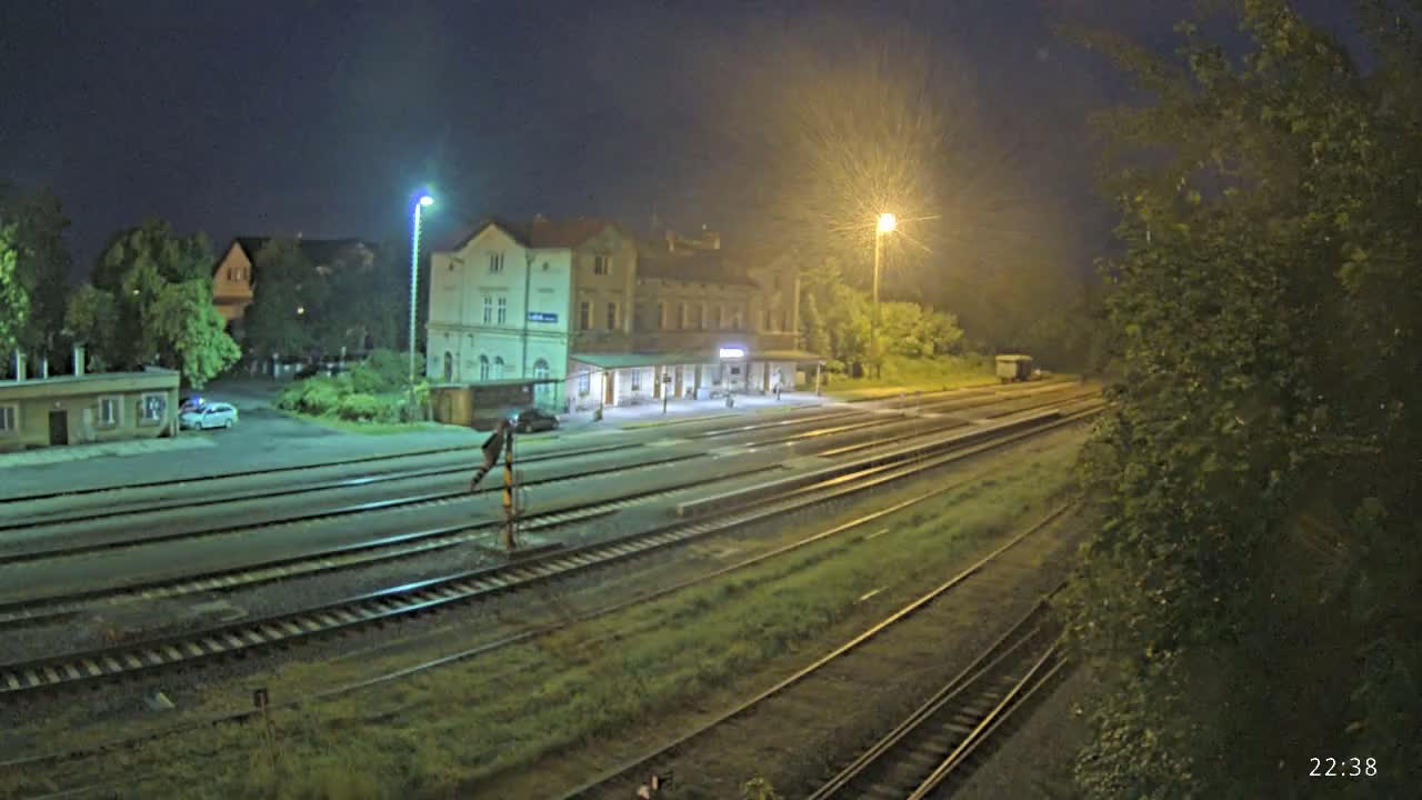 A nighttime view of a train station with several sets of train tracks extending into the distance, under partly cloudy skies.