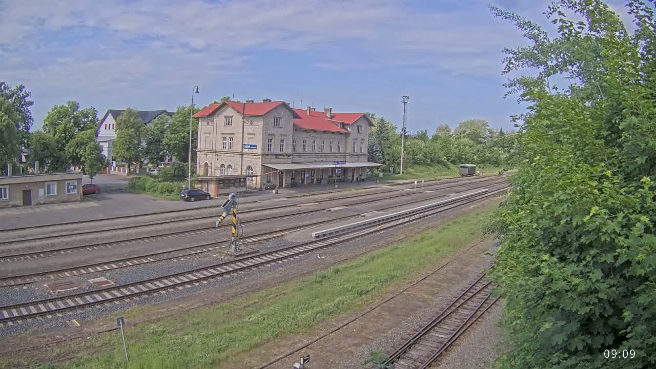 A long view of a train station with a red-roofed building and several train tracks under a partly cloudy sky.