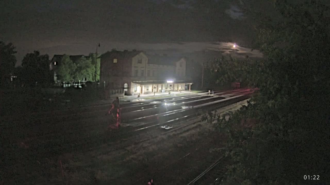 A dimly lit train station at night under a partly cloudy sky with a visible moon.
