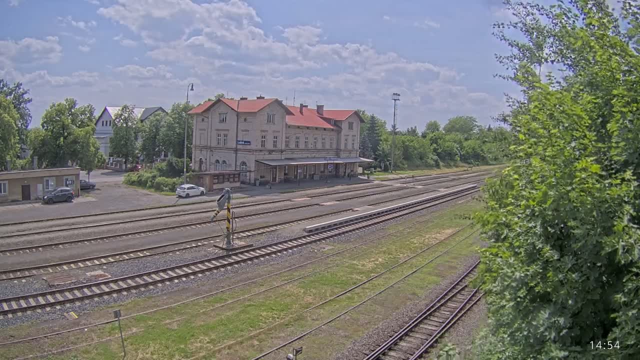 A train station with a long platform and multiple train tracks, under a partly cloudy sky.