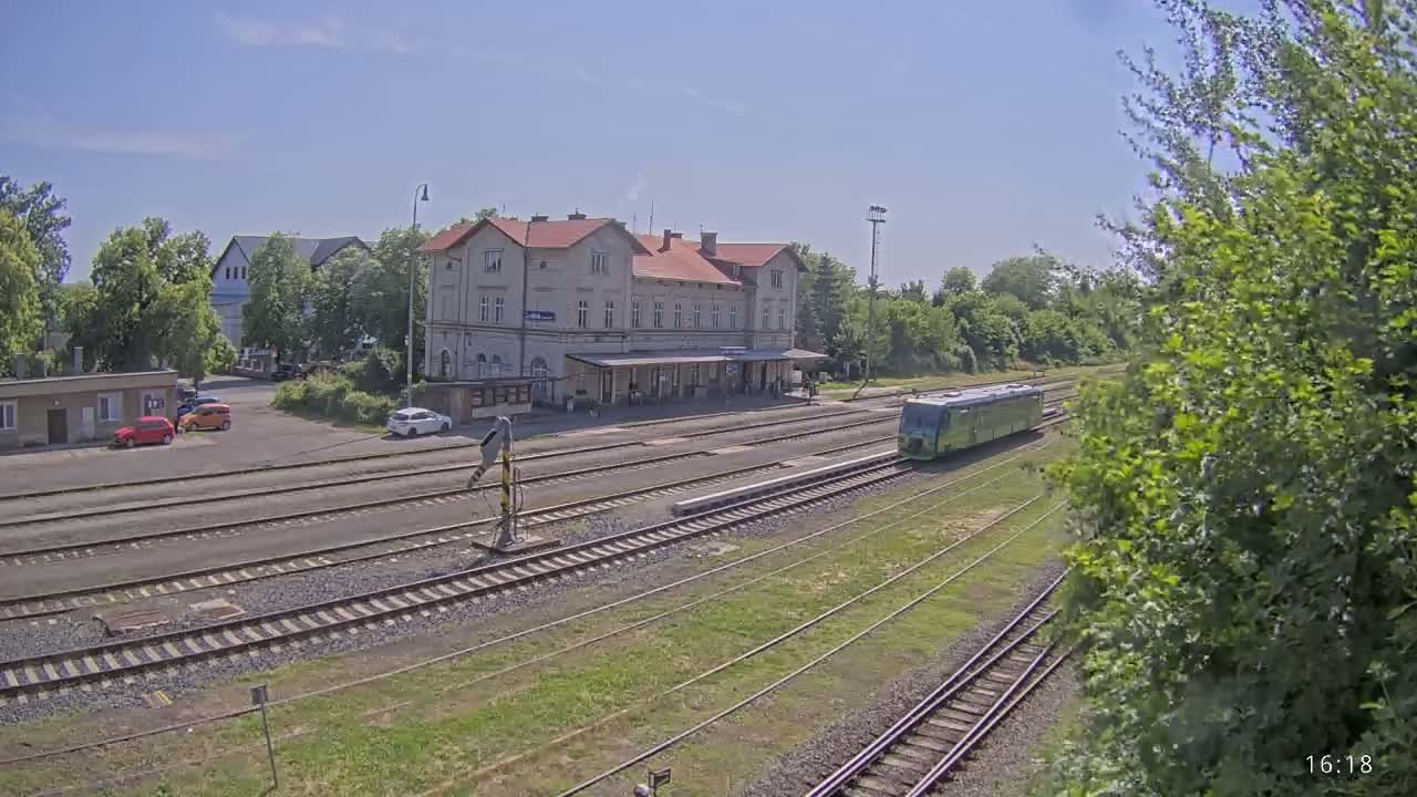 A light-green train is at a train station on a sunny day, with several cars parked nearby.