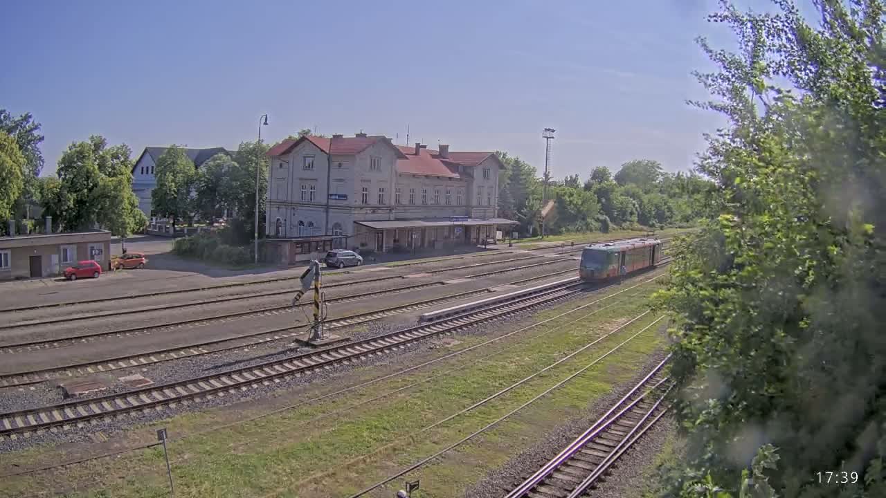 A train passes by a long, light-colored train station on a sunny day.