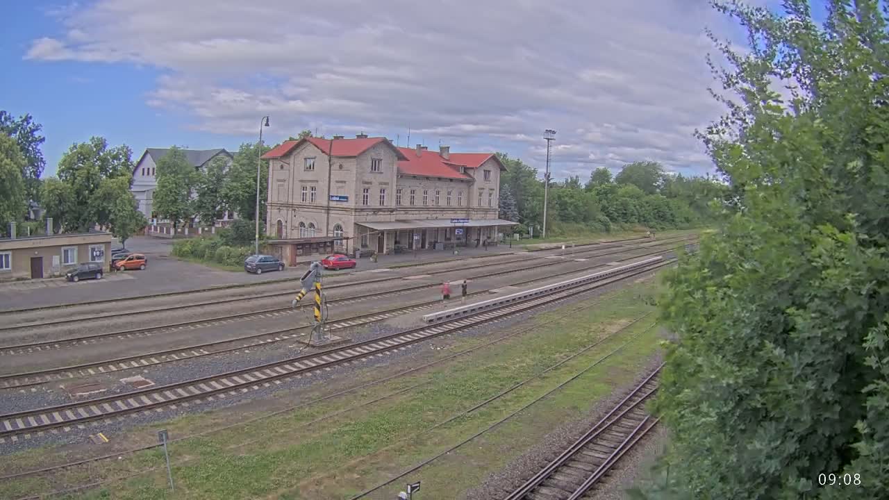 A train station with a long building and several train tracks under partly cloudy skies.