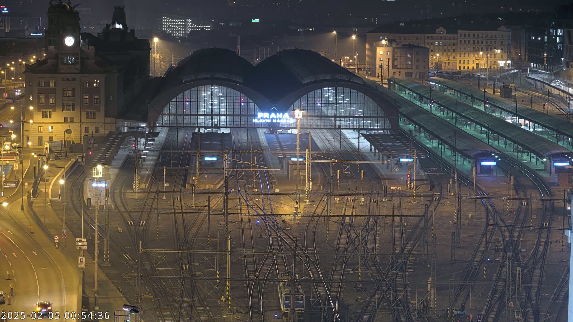 A nighttime aerial view of a large, illuminated train station with many tracks and platforms.