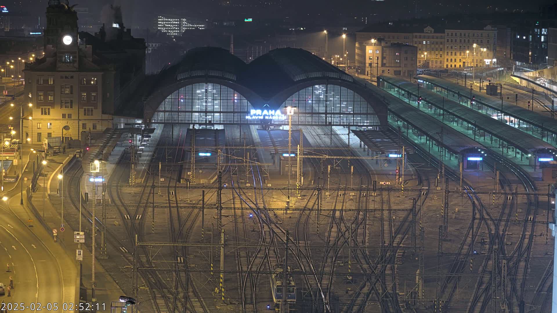 A large, illuminated train station at night, with a complex network of train tracks surrounding it.