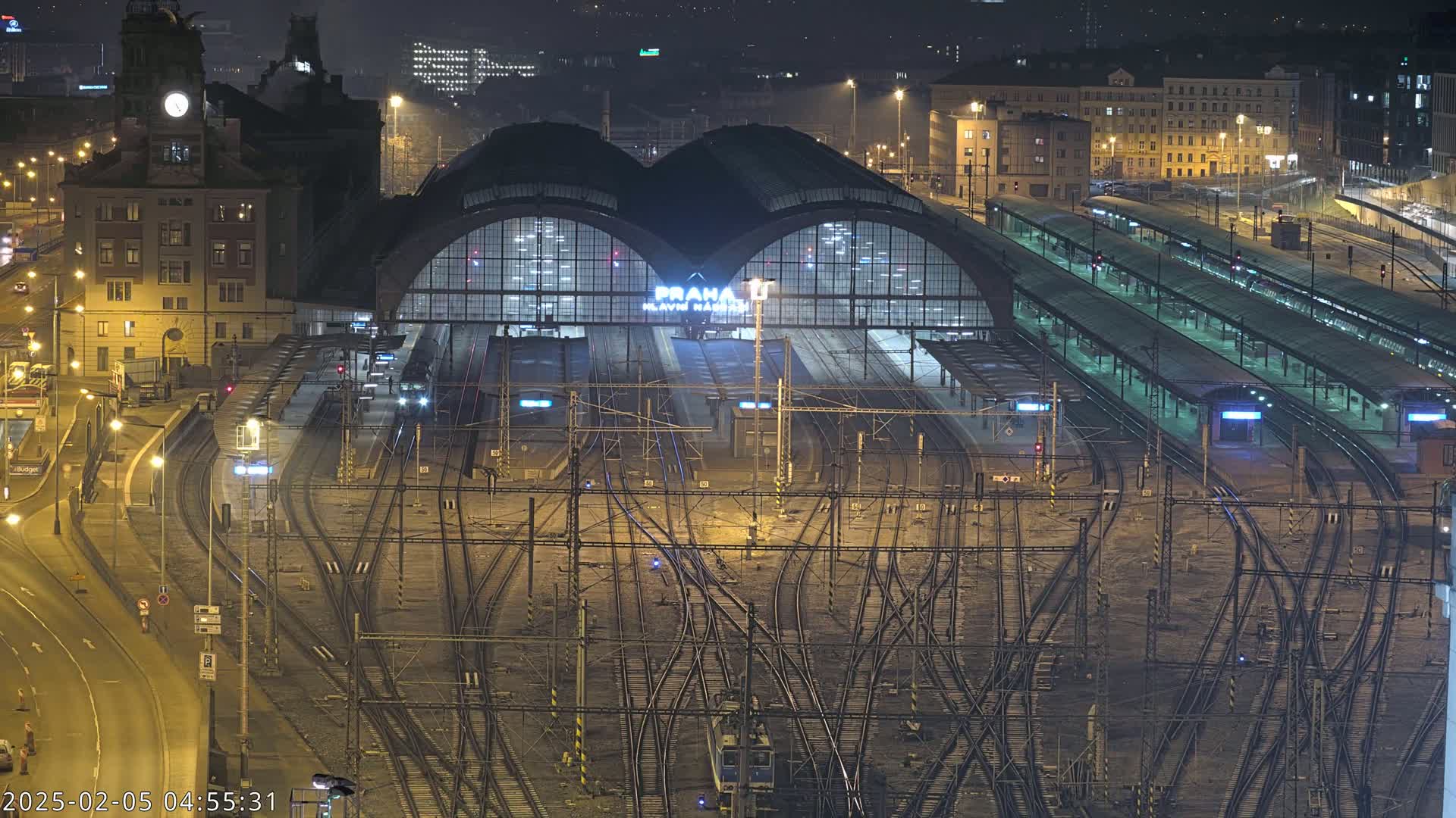 A nighttime aerial view of a large train station with numerous tracks and platforms, illuminated under city lights.