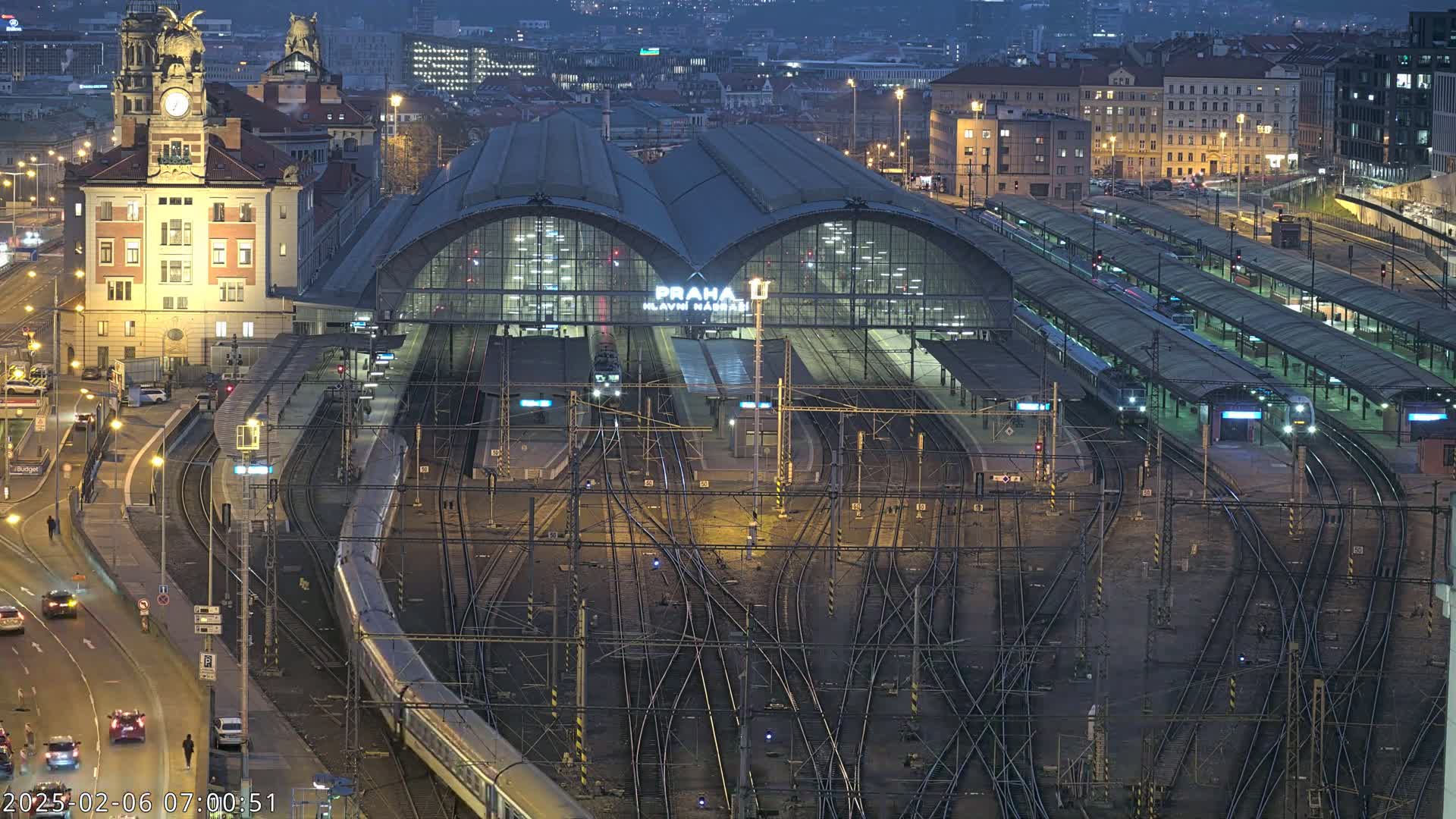 A large train station at night, with many trains at the platforms and a complex network of tracks, under a dark sky.