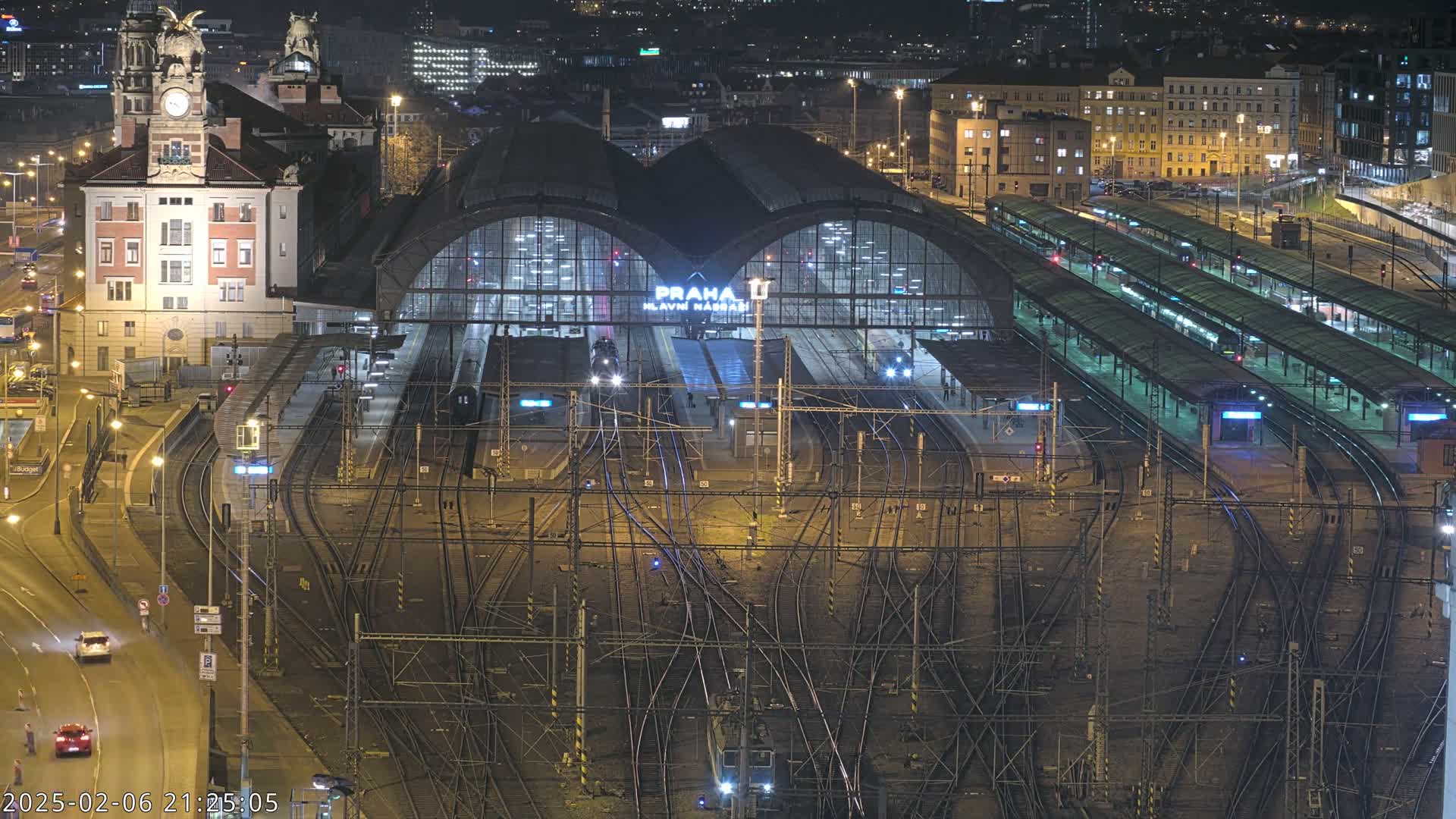 A large, illuminated train station at night with numerous tracks and platforms, surrounded by city buildings.