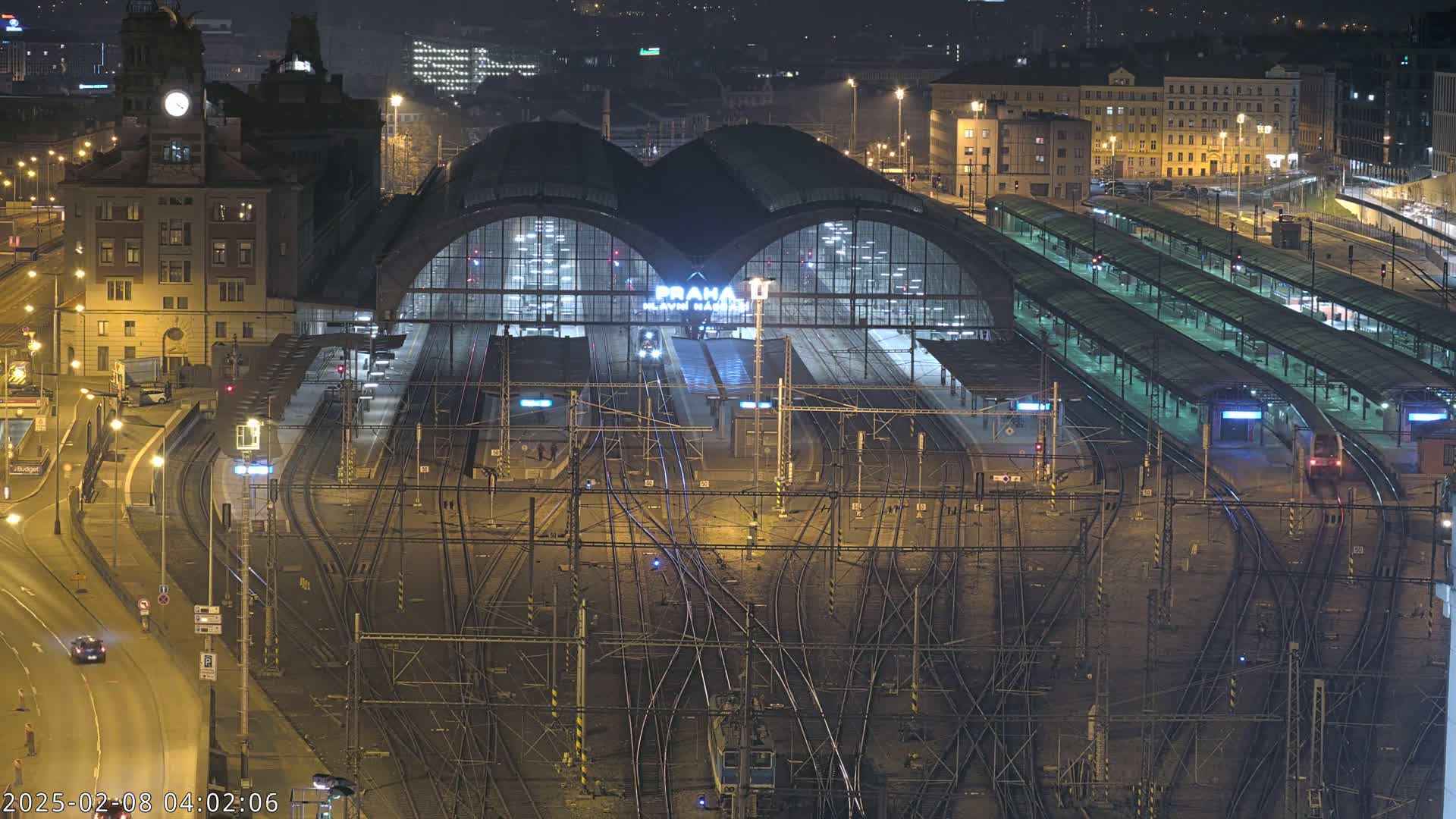 A nighttime aerial view of a large, illuminated train station with numerous tracks and platforms.