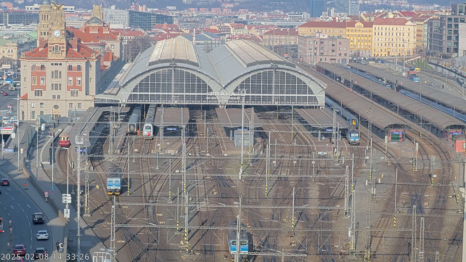 A large train station with numerous tracks and trains, situated in a city under a clear sky.