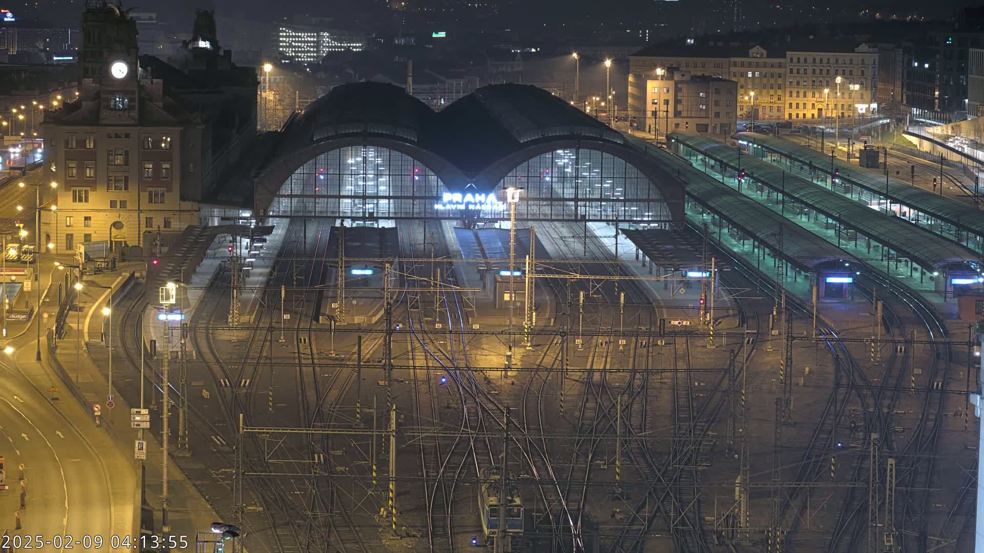 A nighttime aerial view of a large train station with numerous tracks and platforms, illuminated by artificial lights.
