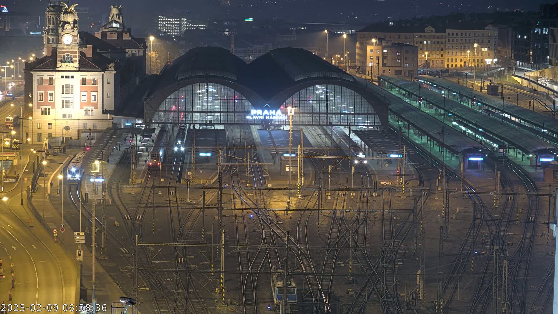 A nighttime, aerial view of a large, illuminated train station with numerous tracks and trains.